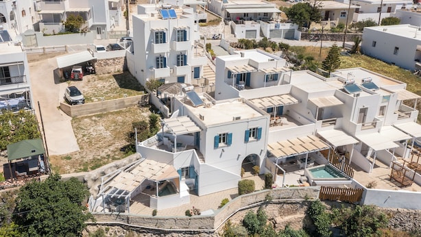 A residential area with modern white buildings, a swimming pool, and a small garden. -  Vivere Houses (Milos)