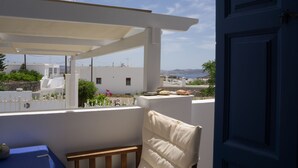 A balcony with a white chair and a table, overlooking a coastal area with buildings and a clear sky. -  Vivere Houses (Milos)