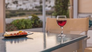 A table with a plate of food and a glass of red wine, a chair, and a view of buildings and greenery. -  Vivere Houses (Milos)