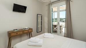 A hotel room with a bed, a TV, a desk, a mirror, and a balcony with a table and chairs. -  Vivere Houses (Milos)