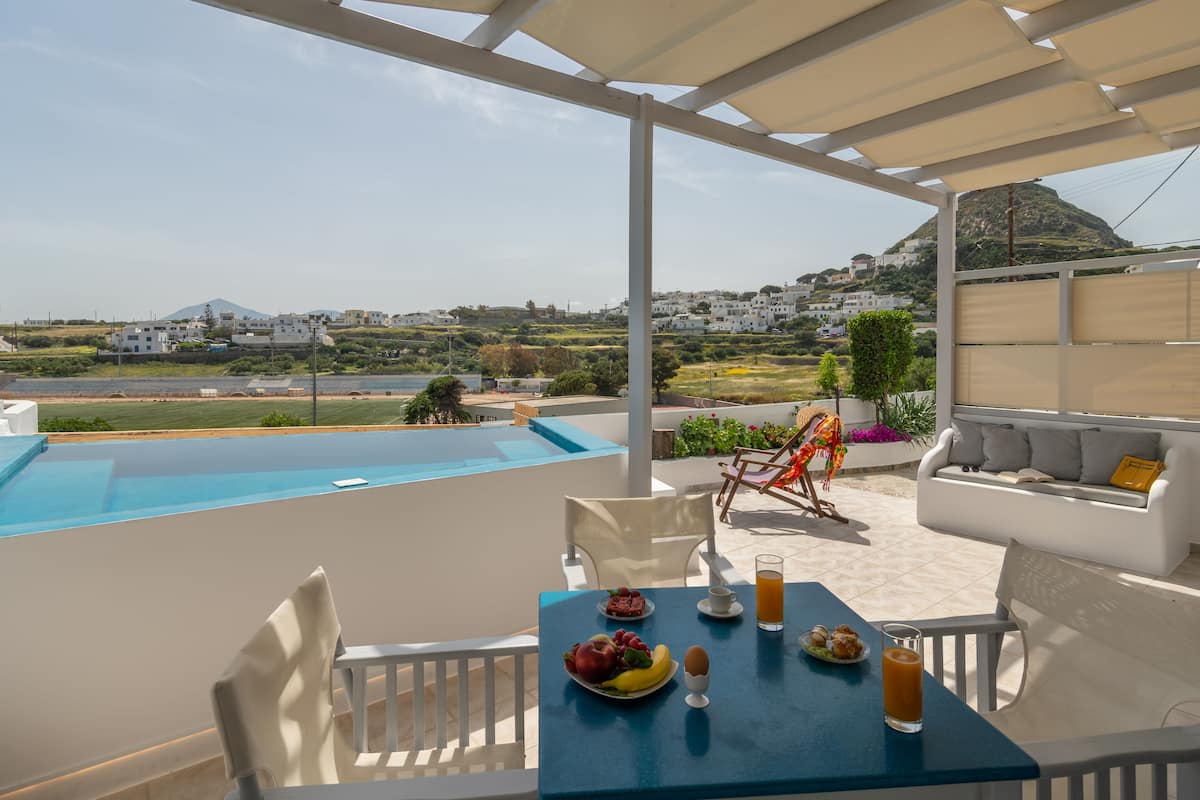A terrace with a pool, outdoor seating, and a table set with breakfast.