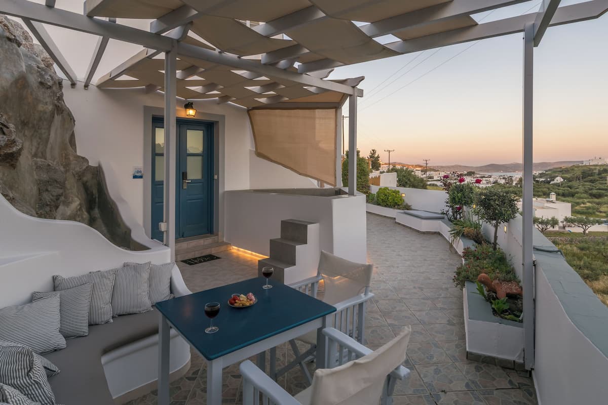 A terrace with a table and chairs, a blue door, and a view of the landscape.
