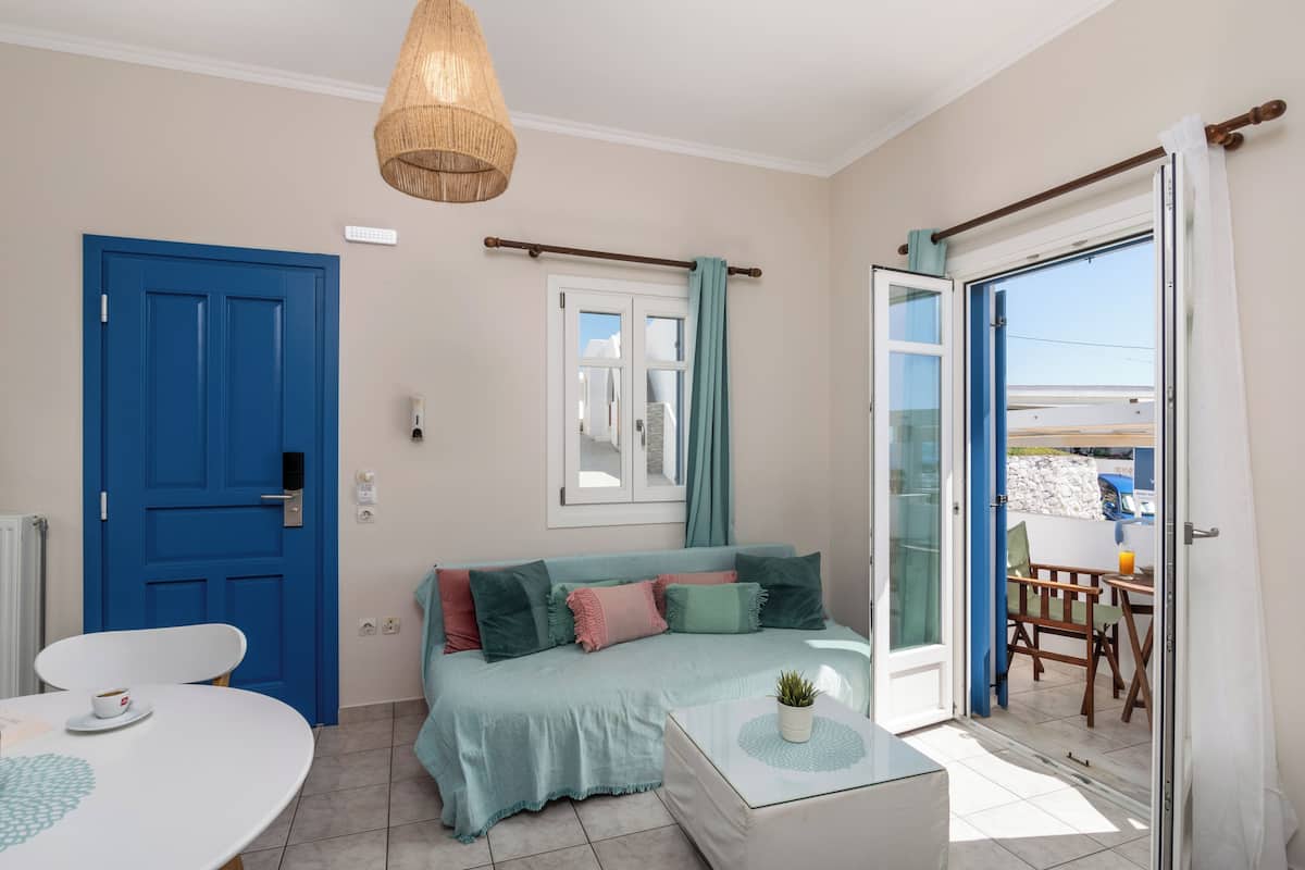 A room with a blue door, a sofa with multiple cushions, a table with a cup, and a view through a glass door.