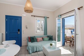 A room with a blue door, a sofa with multiple cushions, a table with a cup, and a view through a glass door.