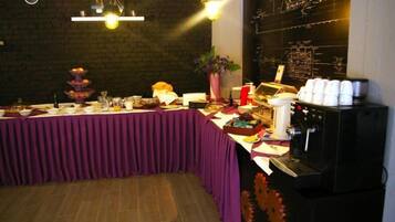 A buffet setup with a purple tablecloth, a coffee machine, and a decorative wall with musical instruments.