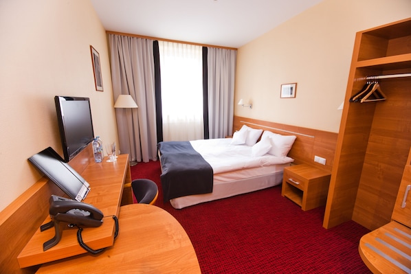 A hotel room with a bed, desk, chair, and wardrobe.