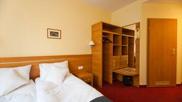 Een hotelkamer met een bed, een houten kledingkast, een klein tafeltje en een afvalbak.