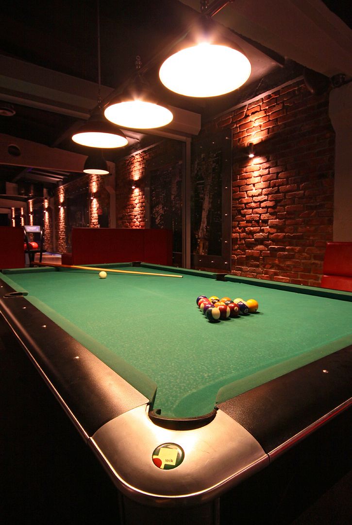 A pool table with balls, a brick wall, and hanging lights.