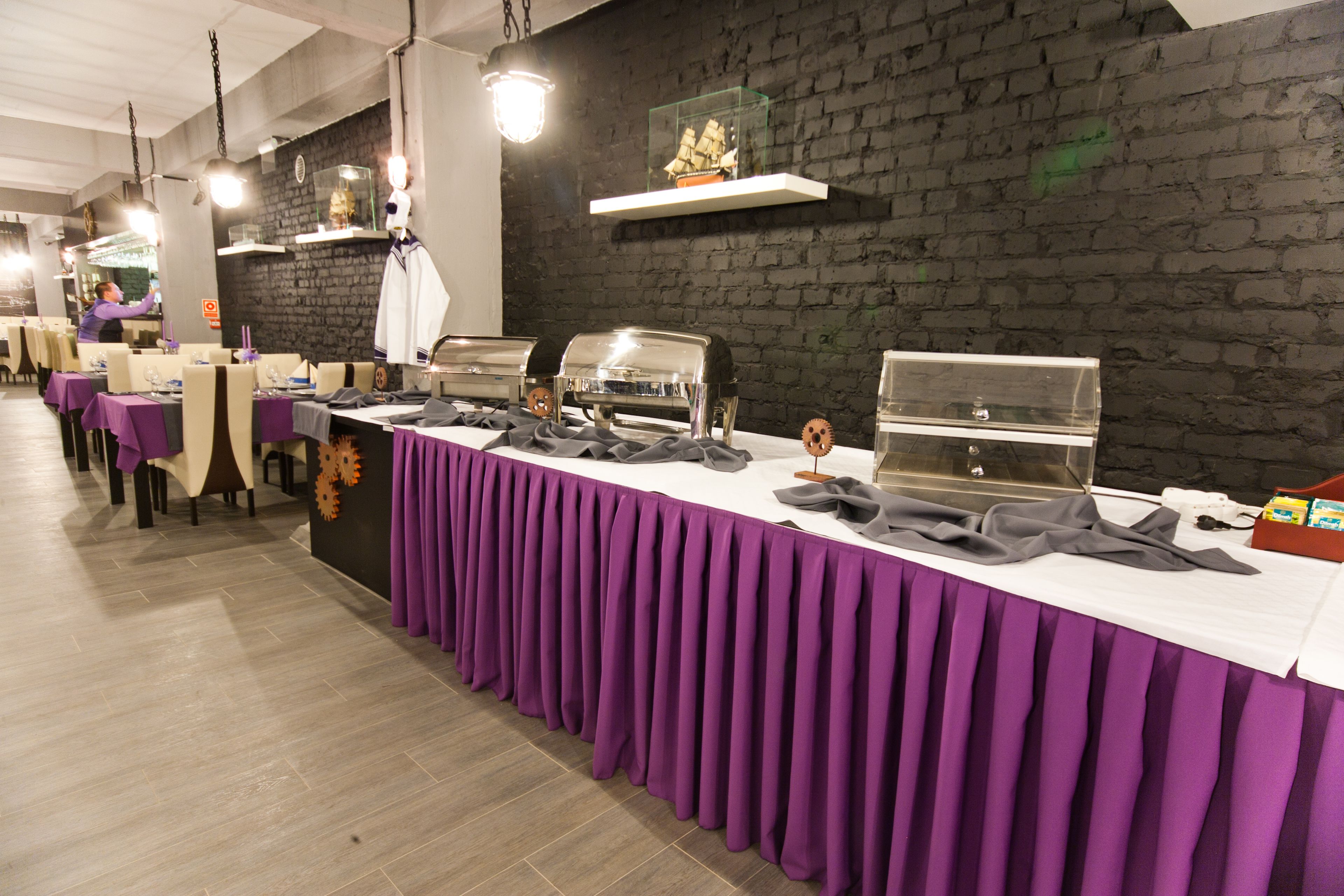 A buffet setup with multiple food stations, a brick wall, and a long table covered with a purple tablecloth.