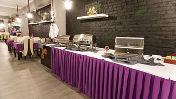 A buffet setup with multiple food stations, a brick wall, and a long table covered with a purple tablecloth.
