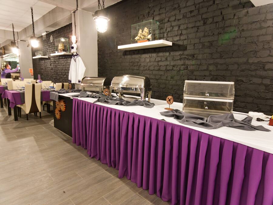 A buffet setup with multiple food stations, a brick wall, and a long table covered with a purple tablecloth.