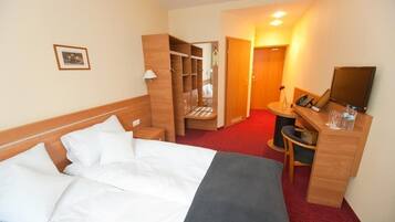 A hotel room with a bed, a desk, a chair, a wardrobe, and a mirror.