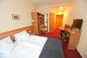 Una habitación de hotel con cama, escritorio, silla, armario y espejo.
