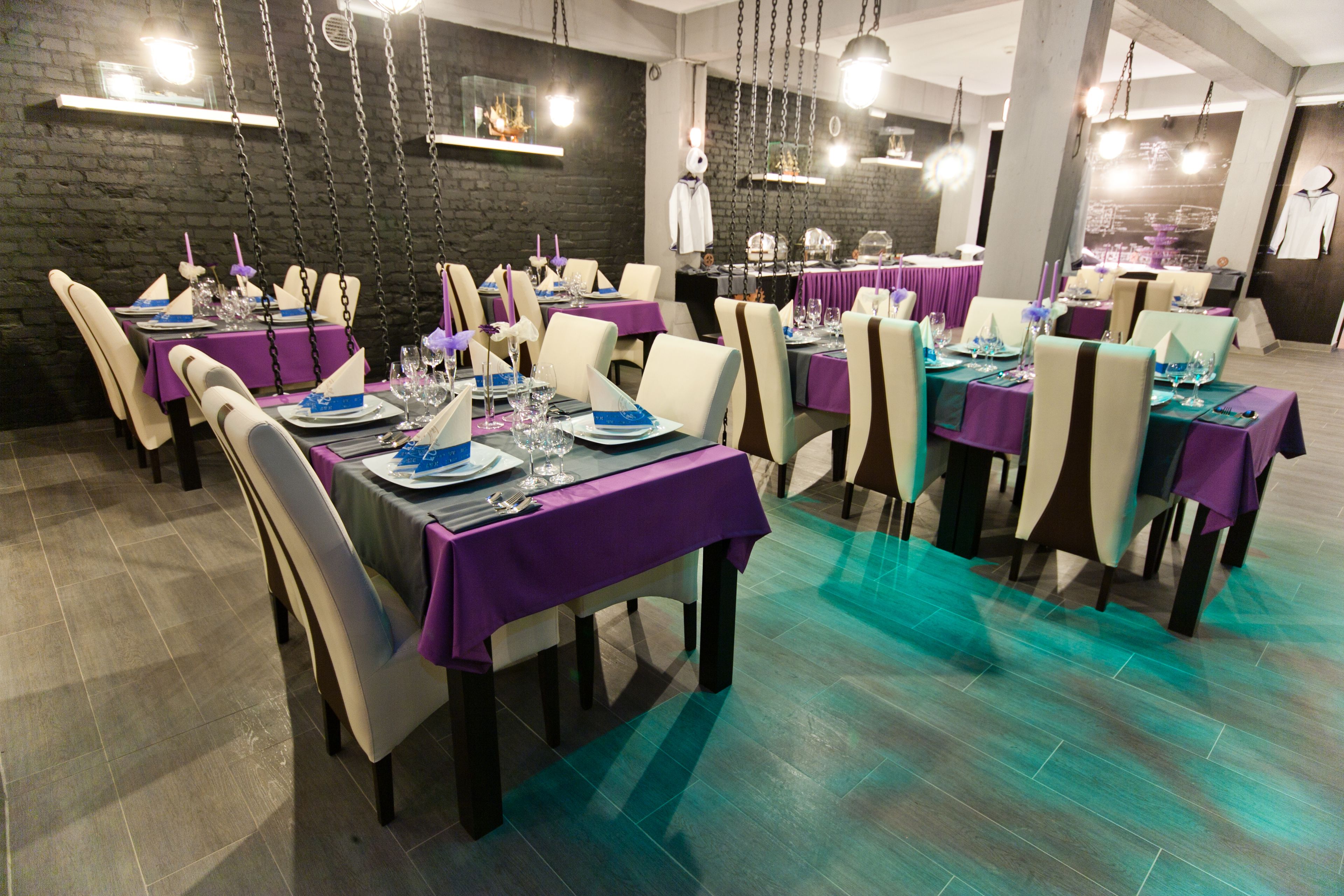 Ein Restaurant mit mehreren Tischen, gedeckt für das Essen, mit lilafarbenen Tischdecken und weißen Stühlen.