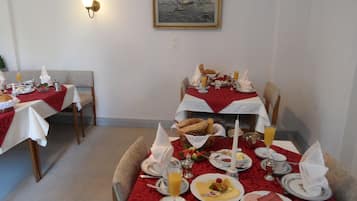 Uma sala de jantar com mesas preparadas para o café da manhã, incluindo pão, ovos e frutas.