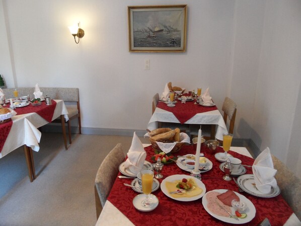 Comedor con mesas preparadas para el desayuno, incluyendo pan, huevos y fruta.