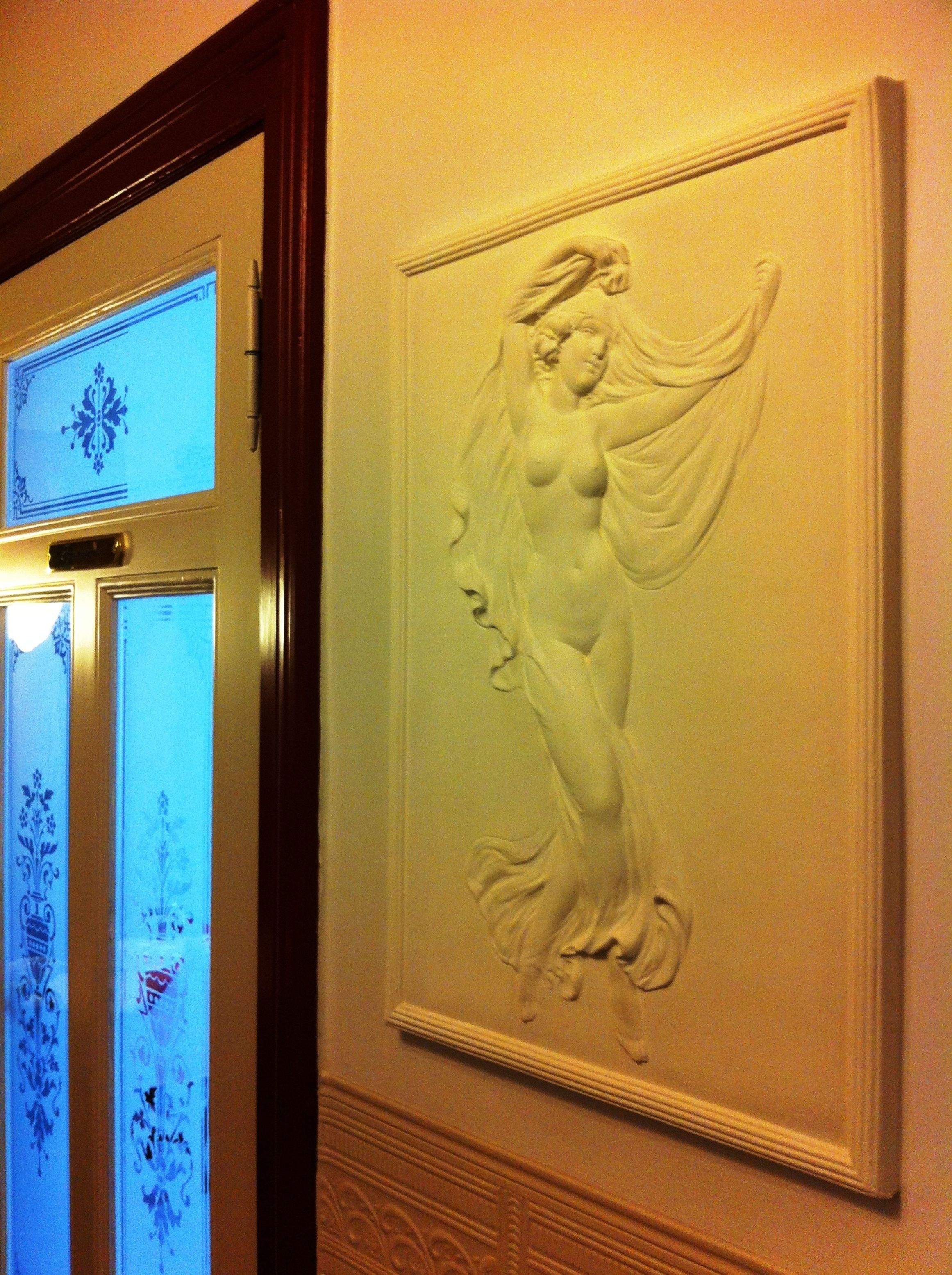 A wall with a relief sculpture of a woman and a door with frosted glass panels.