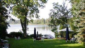A lakeside outdoor seating area with tables and chairs, a covered table, and a boat dock. - Hotel Seeufer (Ploen)