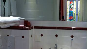 Une salle de bain avec un lavabo blanc, un miroir et une fenêtre ornée de vitraux.