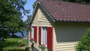 A small, single-story house with a red-tiled roof and a beige exterior. It has a small porch with red shutters and potted plants. - Hotel Seeufer (Ploen)