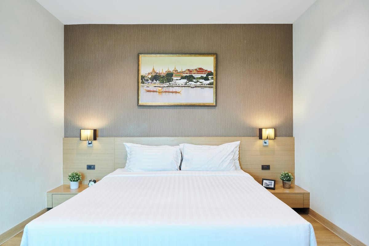 Habitación de hotel con una cama grande, dos mesitas de noche, un cuadro colgado en la pared y dos apliques de luz.