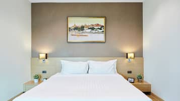 A hotel room with a large bed, two bedside tables, a wall-mounted painting, and two wall sconces.