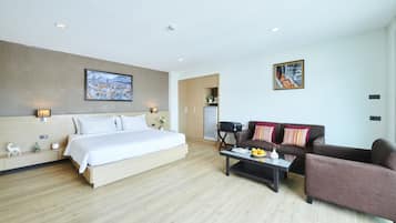 A modern hotel room with a large bed, a sofa, a coffee table, and a desk.