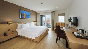 A hotel room with a large bed, a desk with a laptop, a television, and a balcony with a view of buildings. - Adelphi Pattaya (Pattaya)
