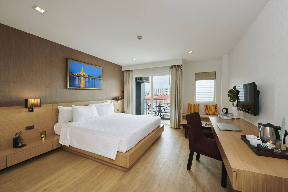 Habitación de hotel con una cama grande, un escritorio con una computadora portátil, televisión y balcón con vistas a edificios.