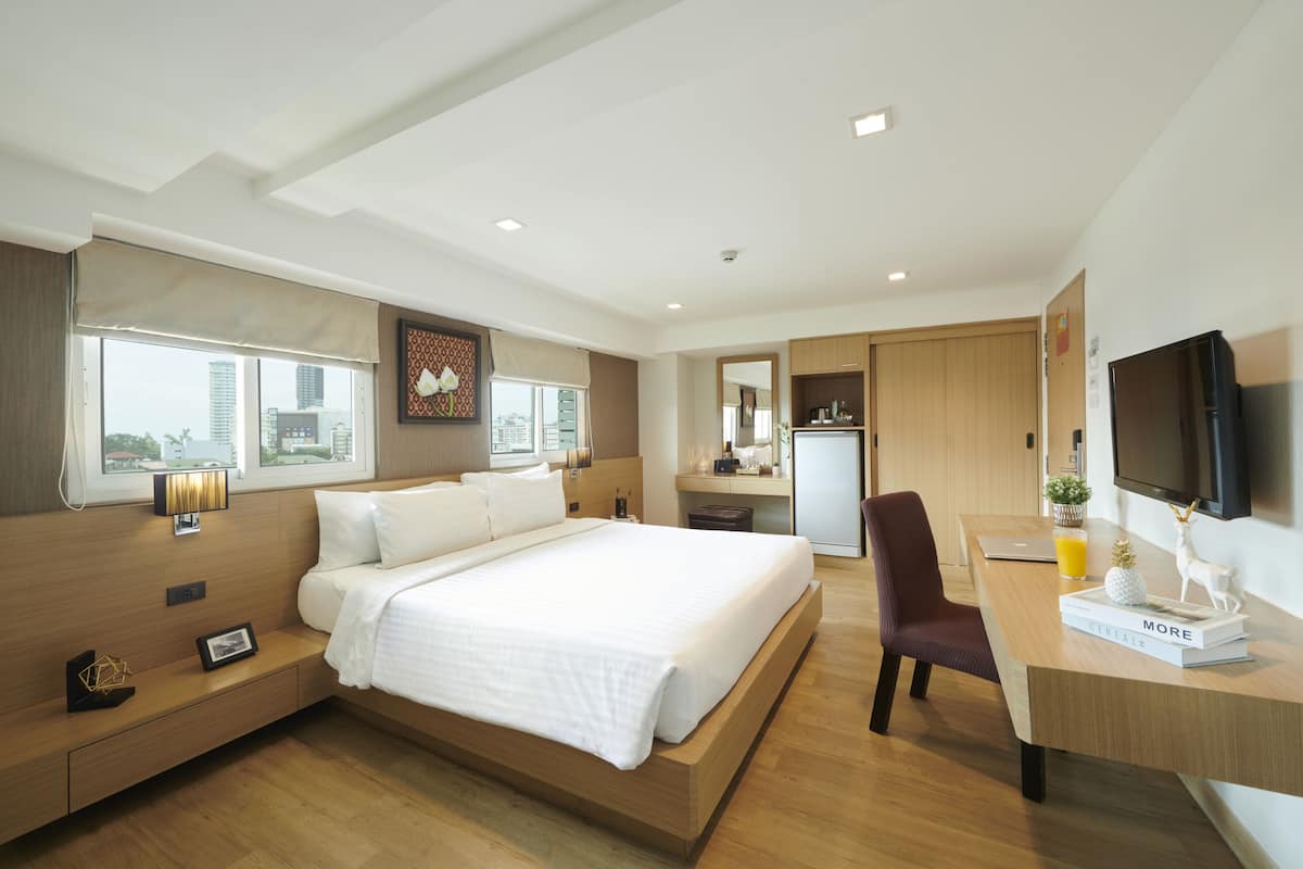 Una habitación de hotel moderna con una cama grande, un escritorio, una silla, un televisor y vistas a la ciudad.