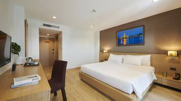 A modern hotel room with a large bed, a desk with a book, a chair, and a painting on the wall.