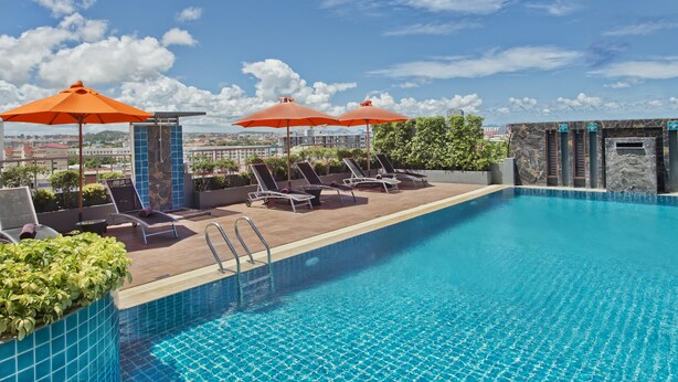 A rooftop pool with lounge chairs and orange umbrellas, surrounded by greenery and city views. - Adelphi Pattaya (Pattaya)