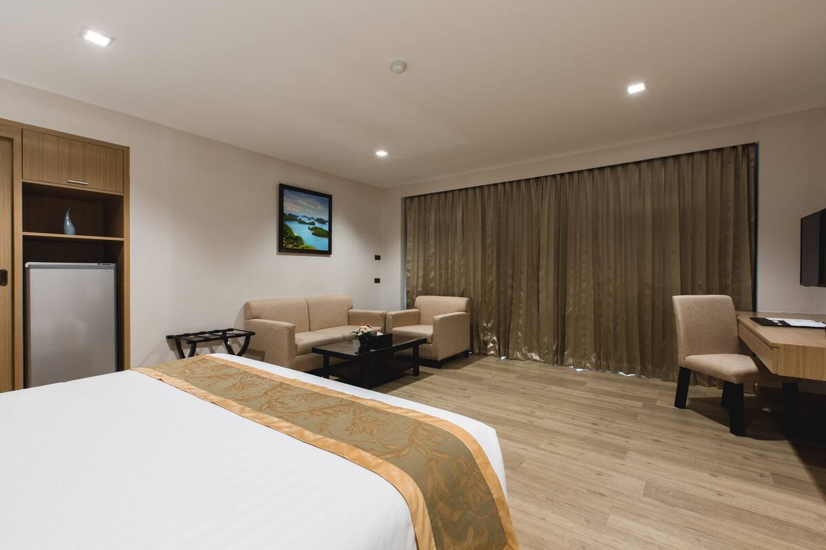 Habitación de hotel con cama, dos sillones, escritorio, mesita de café, televisor y un cuadro en la pared.