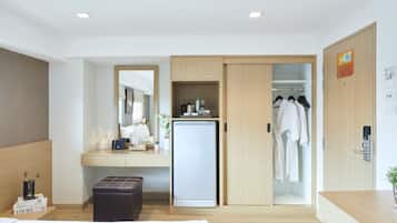 A hotel room with a bed, a desk with a refrigerator, a wardrobe, and a mirror.