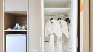 A hotel room with a minibar, a refrigerator, and a wardrobe with hanging robes. - Adelphi Pattaya (Pattaya)