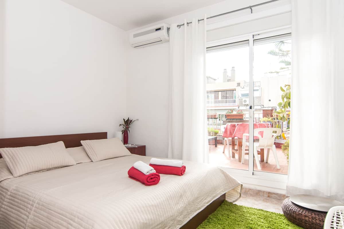 A hotel room with a bed, a nightstand, a potted plant, and a view of the outdoor patio area.