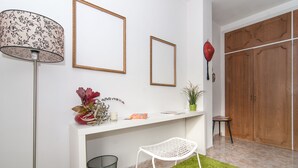 A room with a white console table, a white chair, a floor lamp, a potted plant, and a wooden wardrobe. - The Sky Dome (Barcelona)