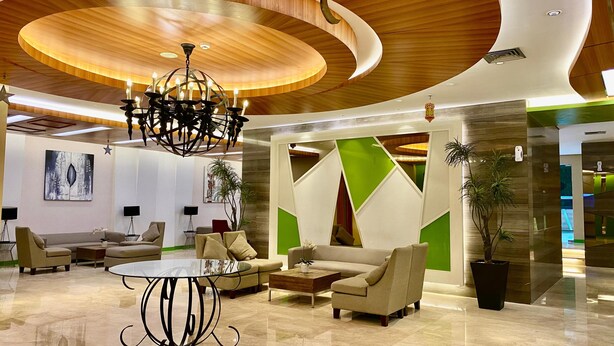 Eine moderne Lobby mit gewölbter Holzdachkonstruktion, einem Kronleuchter und einer Sitzecke mit Sofas und einem Couchtisch.