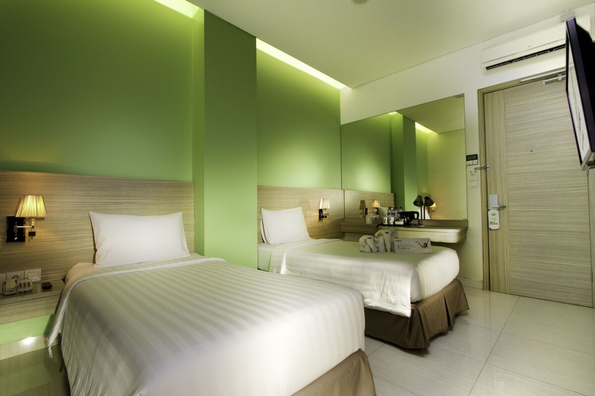 Une chambre d’hôtel avec deux lits, une salle de bain avec un miroir et une armoire.