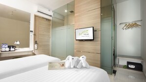 Ein Hotelzimmer mit zwei Betten, einem an der Wand befestigten Fernseher und einem Spiegel. Auf dem Bett liegen weiche Kuscheltiere und an der Wand ist ein Handtuchhalter angebracht.