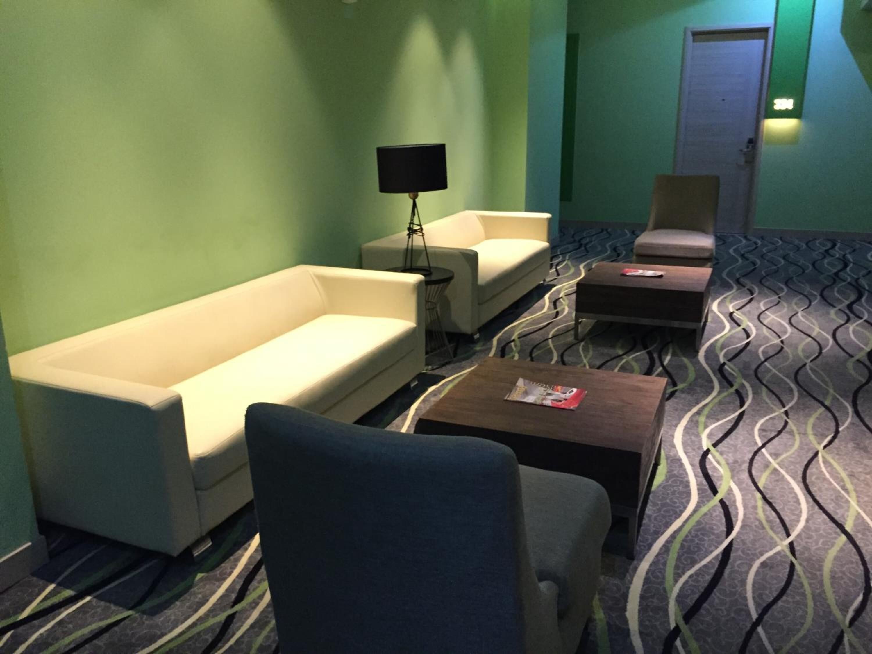 A hotel room with a sofa, armchair, and a small table with a magazine. There is a lamp and a door in the background.