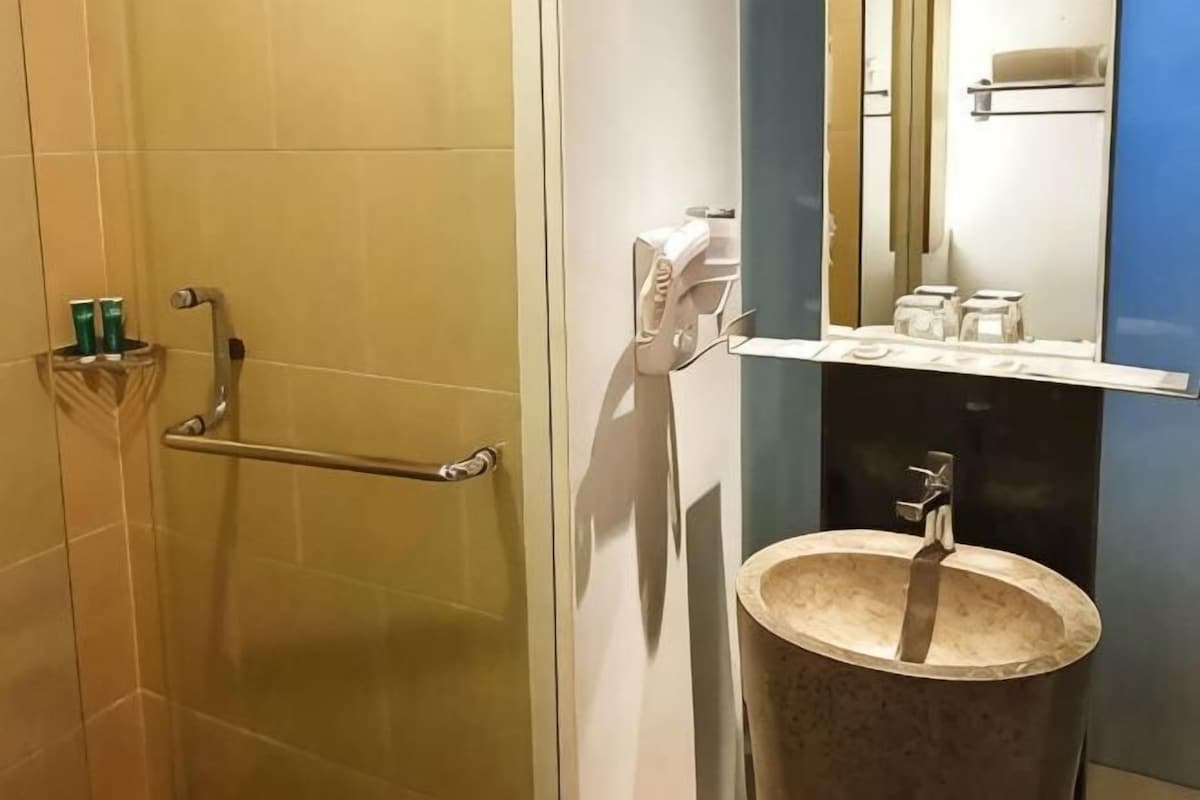 Une salle de bain dotée d’une porte de douche en verre, d’une barre d’appui, d’un lavabo avec un receveur en marbre et d’un miroir avec un porte-serviettes.