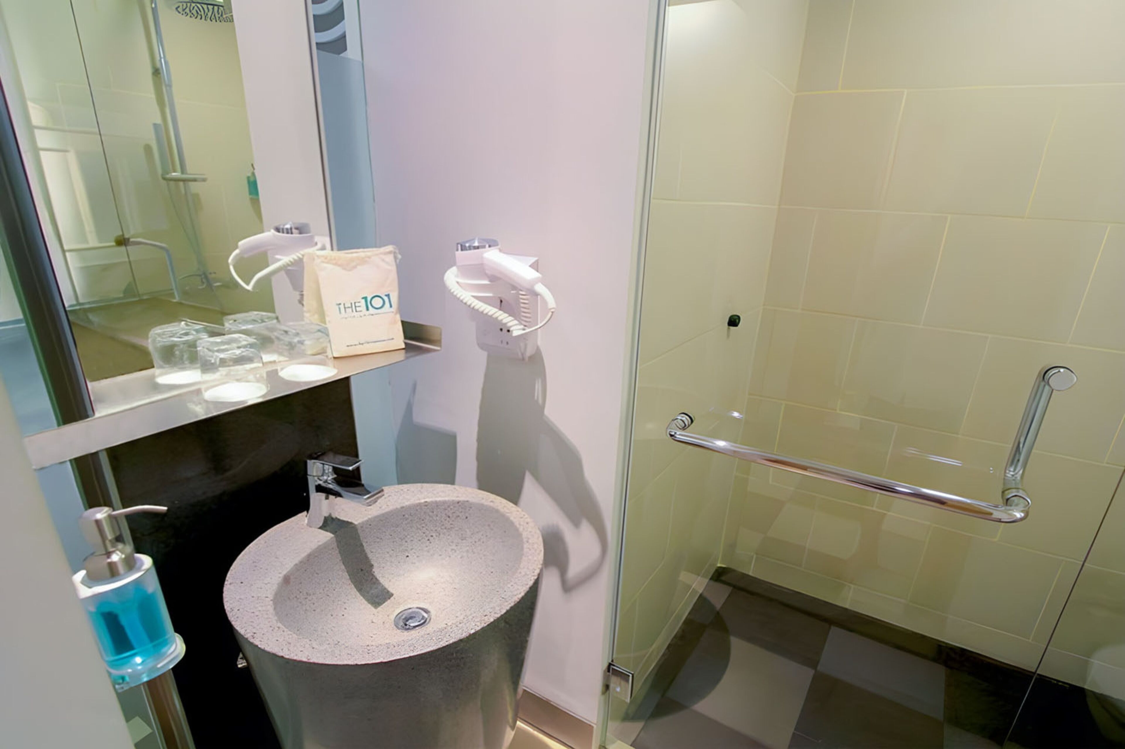 A modern bathroom with a freestanding sink, a glass shower enclosure, and a handrail.