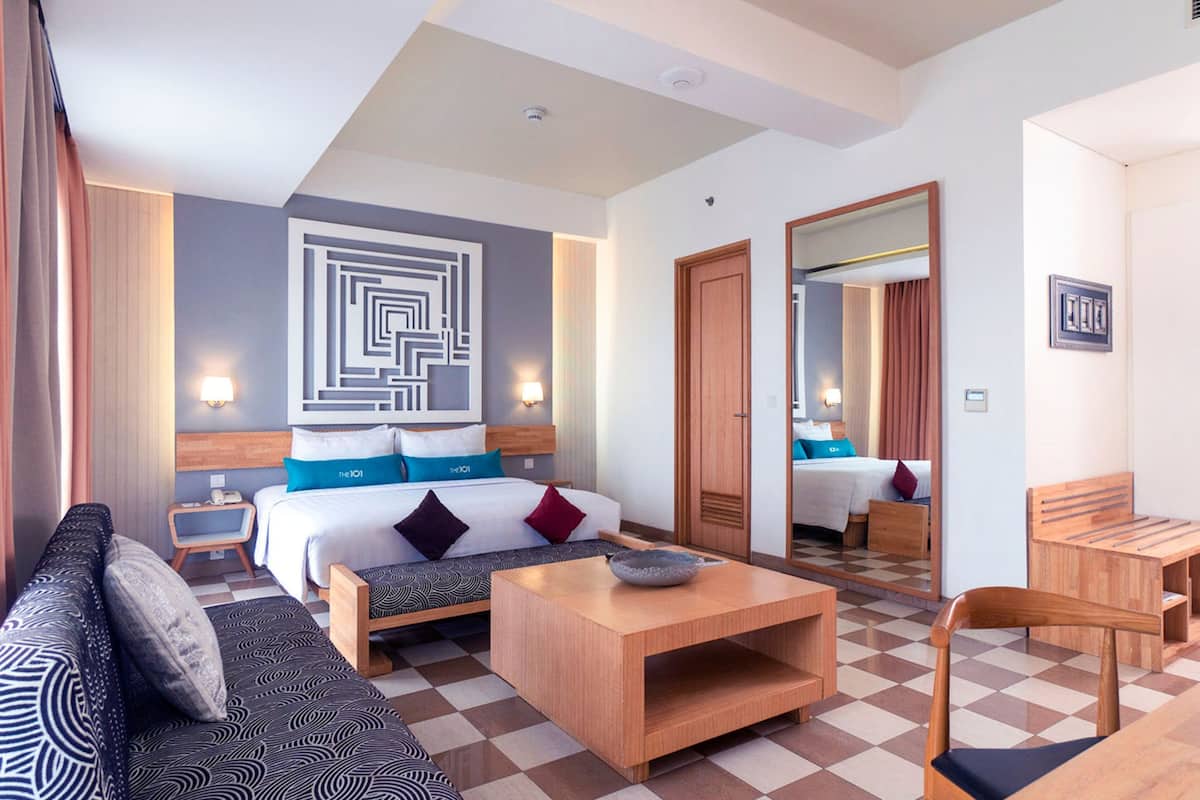 A hotel room with a bed, a sofa, a coffee table, and a dining area.