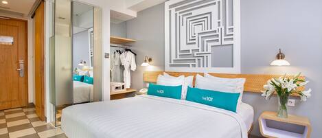 Una habitación de hotel con una cama grande, un armario, un espejo, una mesita de noche con lámpara y una pared con diseño geométrico.