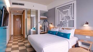 Habitación de hotel con piso a cuadros, una cama grande con ropa de cama blanca y azul, un televisor montado en la pared y un espejo.