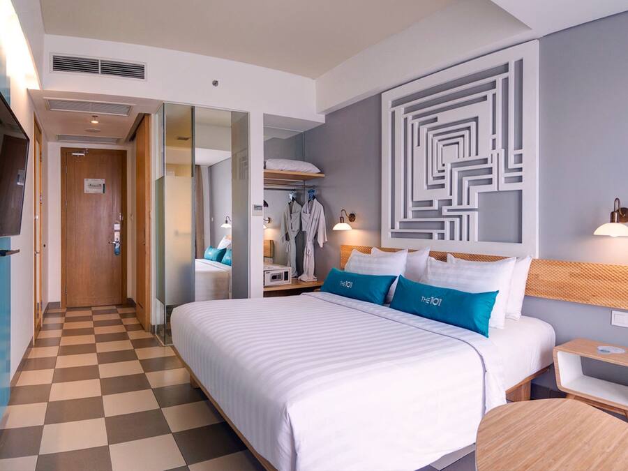 Habitación de hotel con piso a cuadros, una cama grande con ropa de cama blanca y azul, un televisor montado en la pared y un espejo.