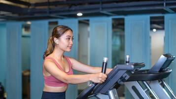 A woman using a stationary bike in a gym with blue walls and visible exercise equipment.