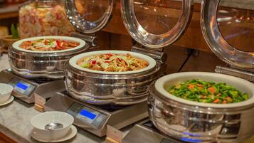 A buffet with various dishes in stainless steel bowls, some with lids, and digital scales for portion control.