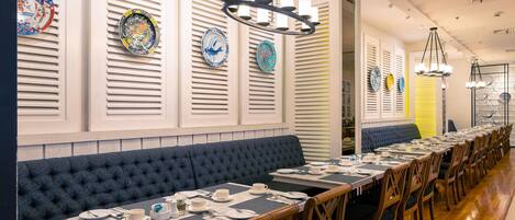 Una larga mesa de comedor con múltiples sillas, un banco acolchado azul y una fila de platos decorativos en la pared.